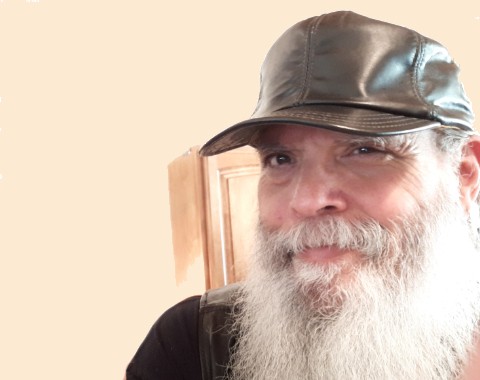 Vibrant image of a cheerful man with a gray beard wearing a leather cap, showcasing creative yarn projects.