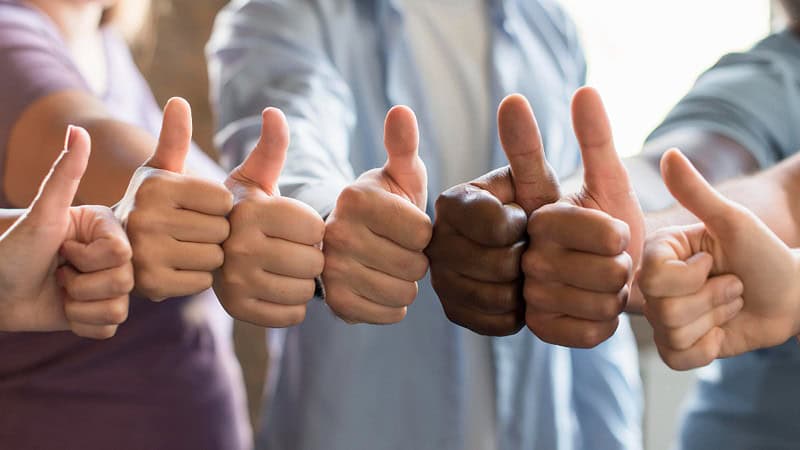 We only the hands of an ethnically diverse group of seven people with outstretched arms and hands giving the thumbs up.