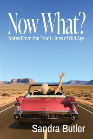 Cover of Now What? Notes From the Front Lines of Old Age by Sandra Butler. A white-haired older woman drives a red vintage convertible down a long desert highway, raising one hand in the air, with mesas in the distance beneath a wide blue sky.